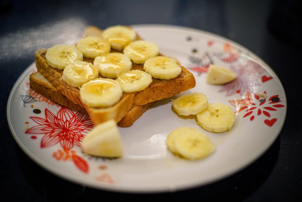 Toast with banana slices and peanut butter sit on a white, floral plate. 
