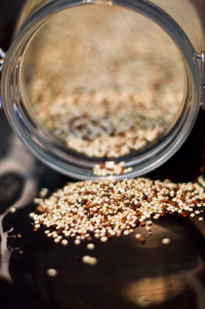 a jar of uncooked quinoa poured out on the table in preparation to make a quinoa kale salad