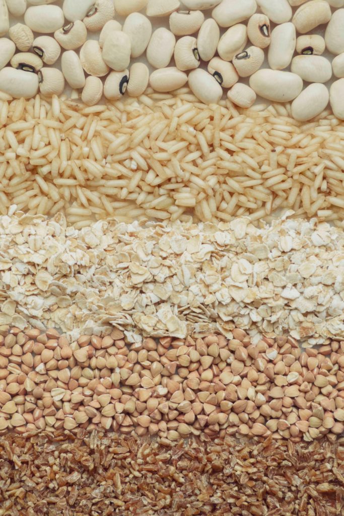 Various whole grains including oatmeal and white rice are laid side by side. 