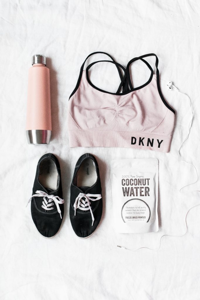 workout outfit for health-related new years resolution. It includes a pink water bottle, sports bra, new tennis shoes, and coconut water powder. 