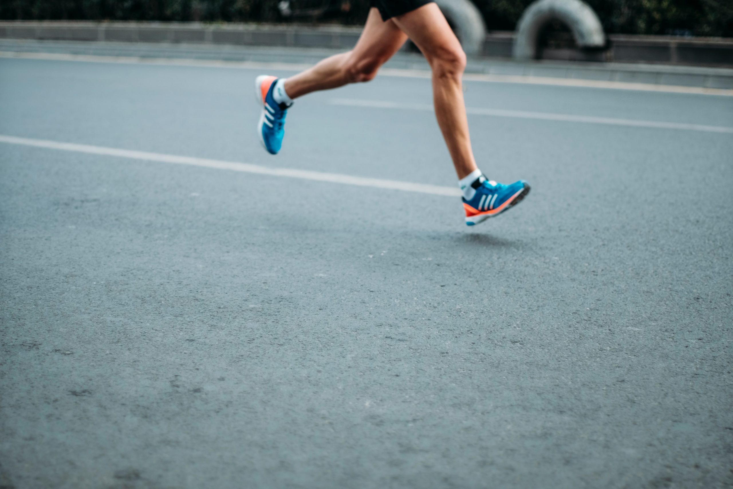 Close-up of a runner's legs in motion wearing blue running shoes on a paved road.