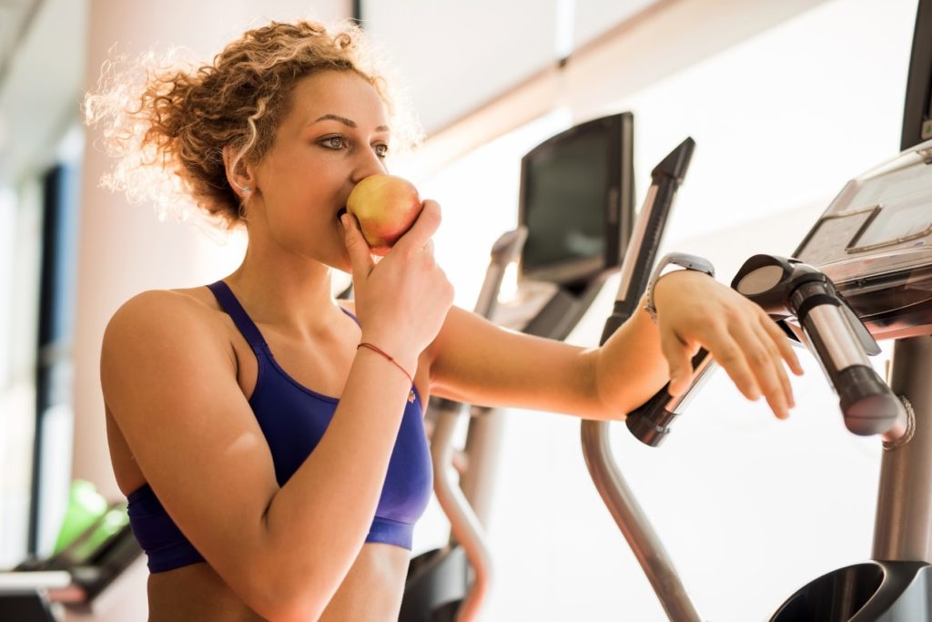Image of female athlete practicing intuitive eating for athletes eating an apple at the gym.