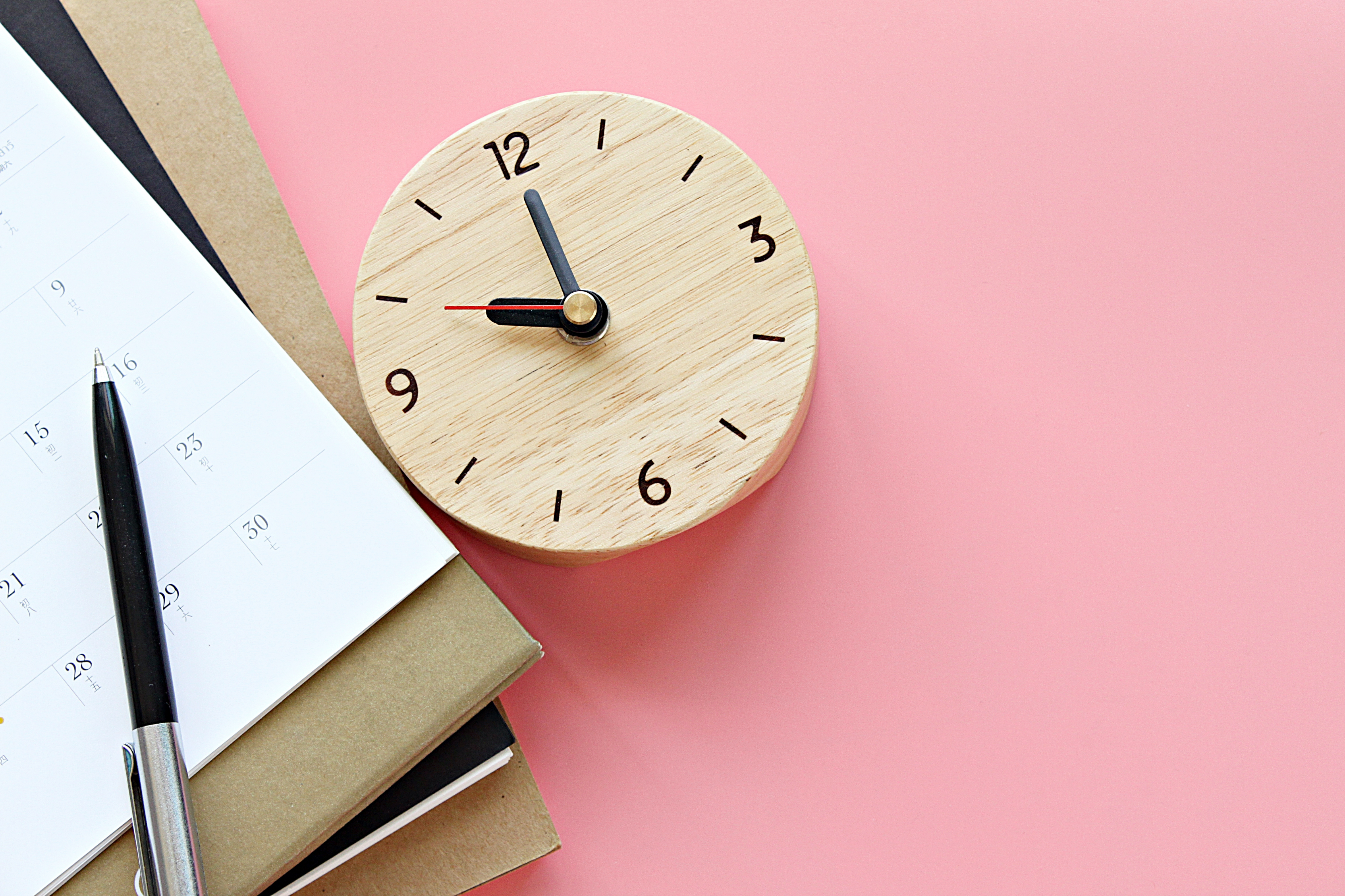 calendar or planner, clock, and pen on a pink background