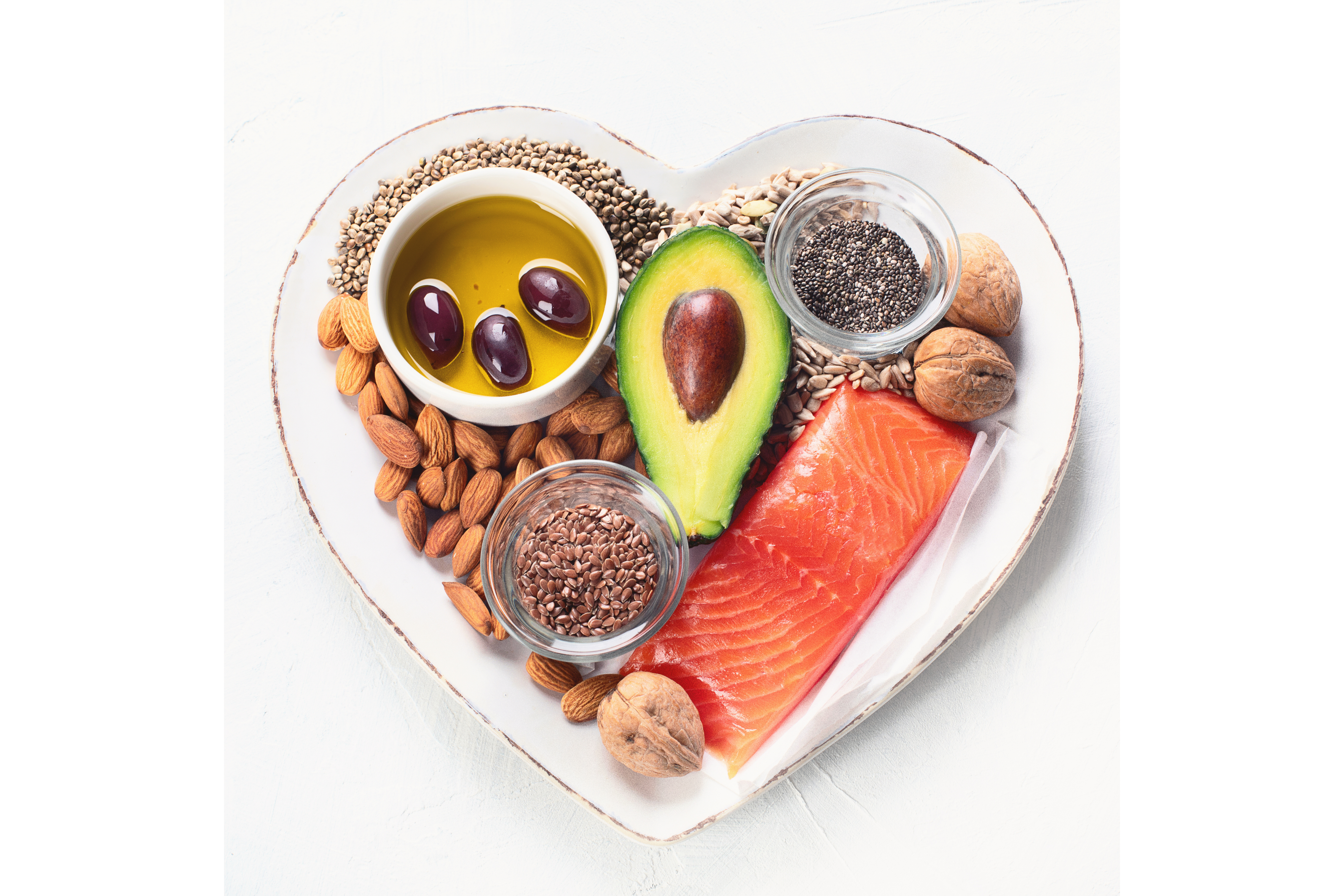 image of various healthy fats in a heart shaped bowl including avocado, olives, nuts, seeds, and salmon