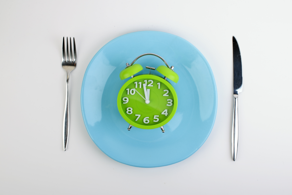 Image of a clock on top of a blue plate with a fork and knife.