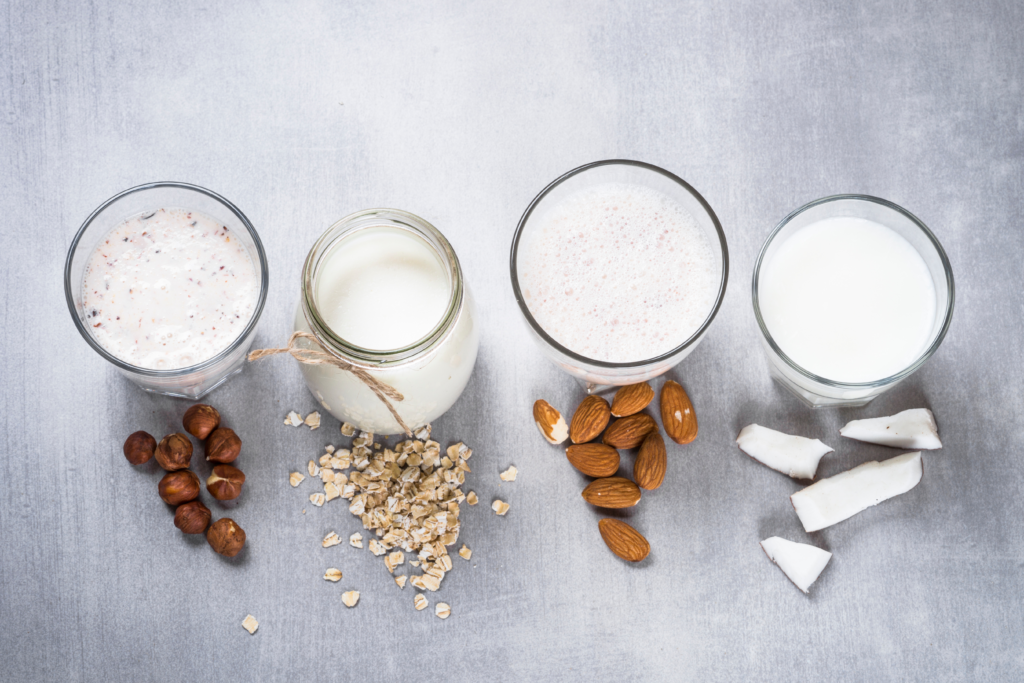 overhead view of different types of milk alternatives in glasses including hazelnut milk, oat milk, almond milk, and coconut milk