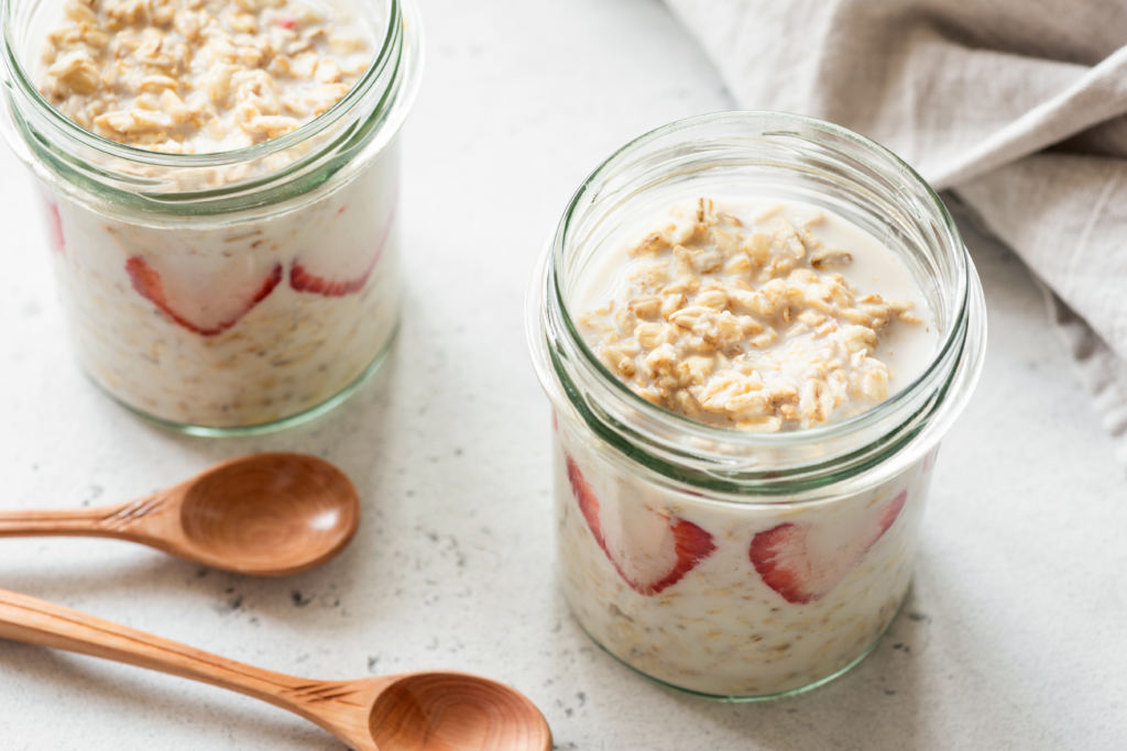 Mason jars of strawberry overnight oats with wooden spoons on a marble countertop