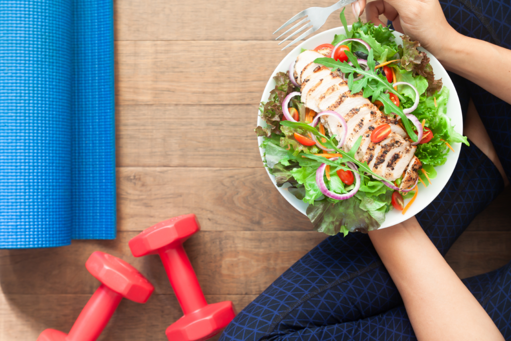 Image of woman eating salad, dumbbells, and a yoga mat.