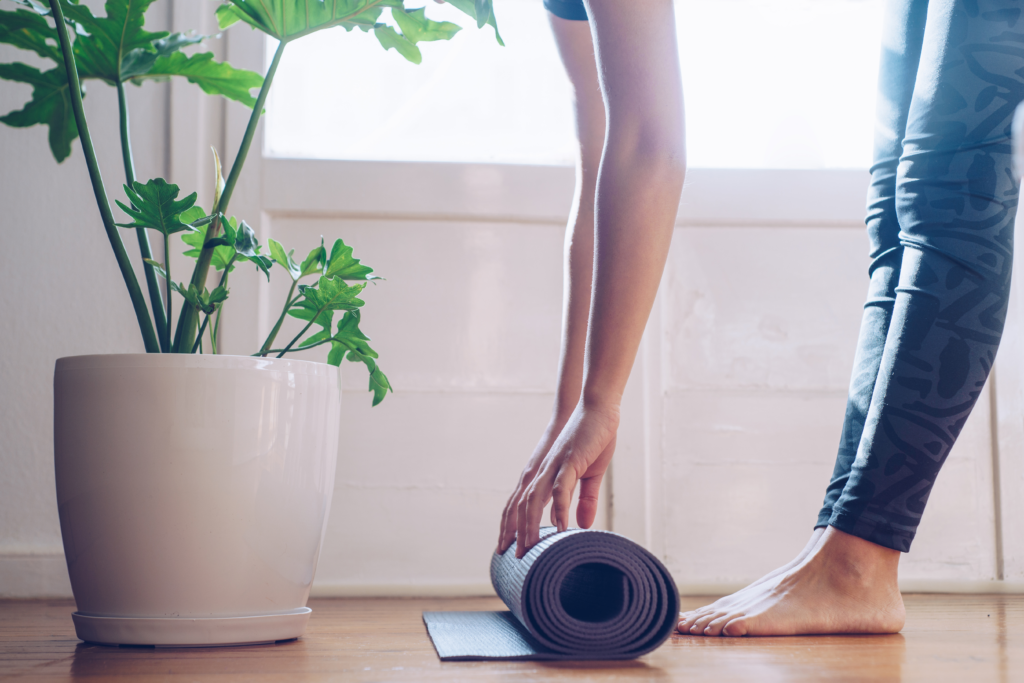 Woman bending over to roll up a yoga mat and a plant 