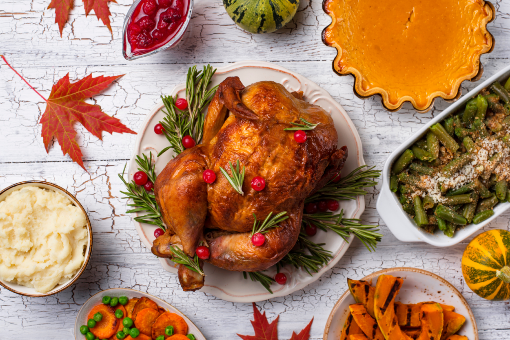 Image of thanksgiving dinner. Turkey in the centre surrounded by other holiday foods like pumpkin pie, mashed potatoes, squash, green beans, and cranberries