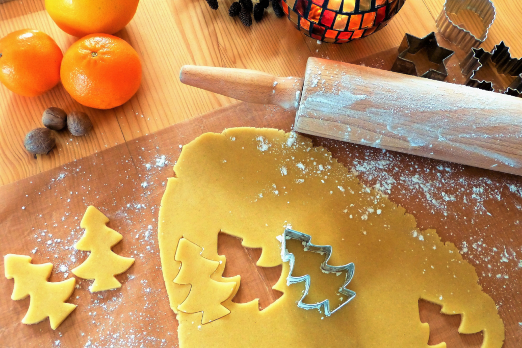 cookie dough on counter with christmas tree cookie cutter, rolling pin, and clementines for the holidays