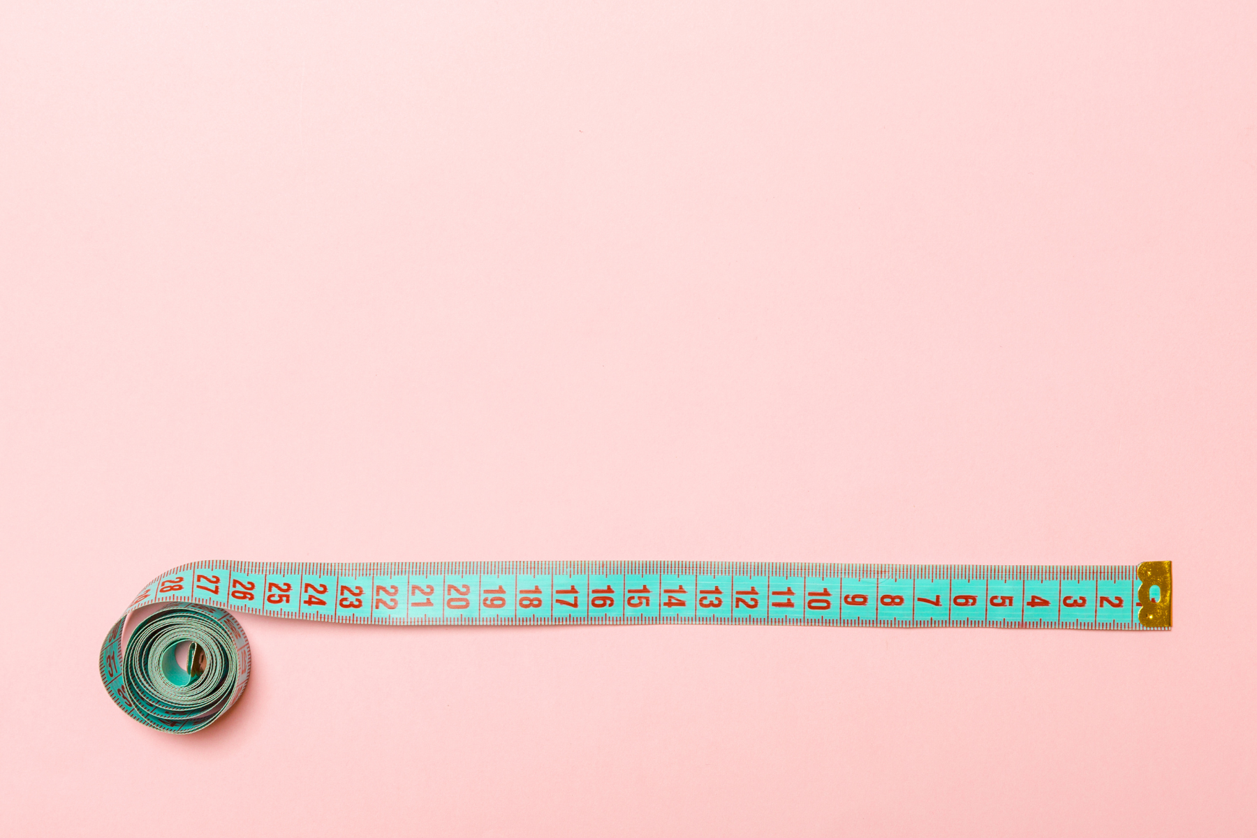 Image of a blue measuring tape that is partially unrolled against a pink background