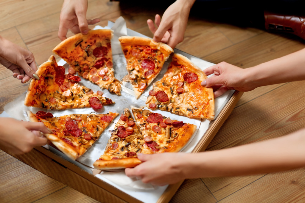 Overhead food image of six hands reaching for pepperoni pizza slices.