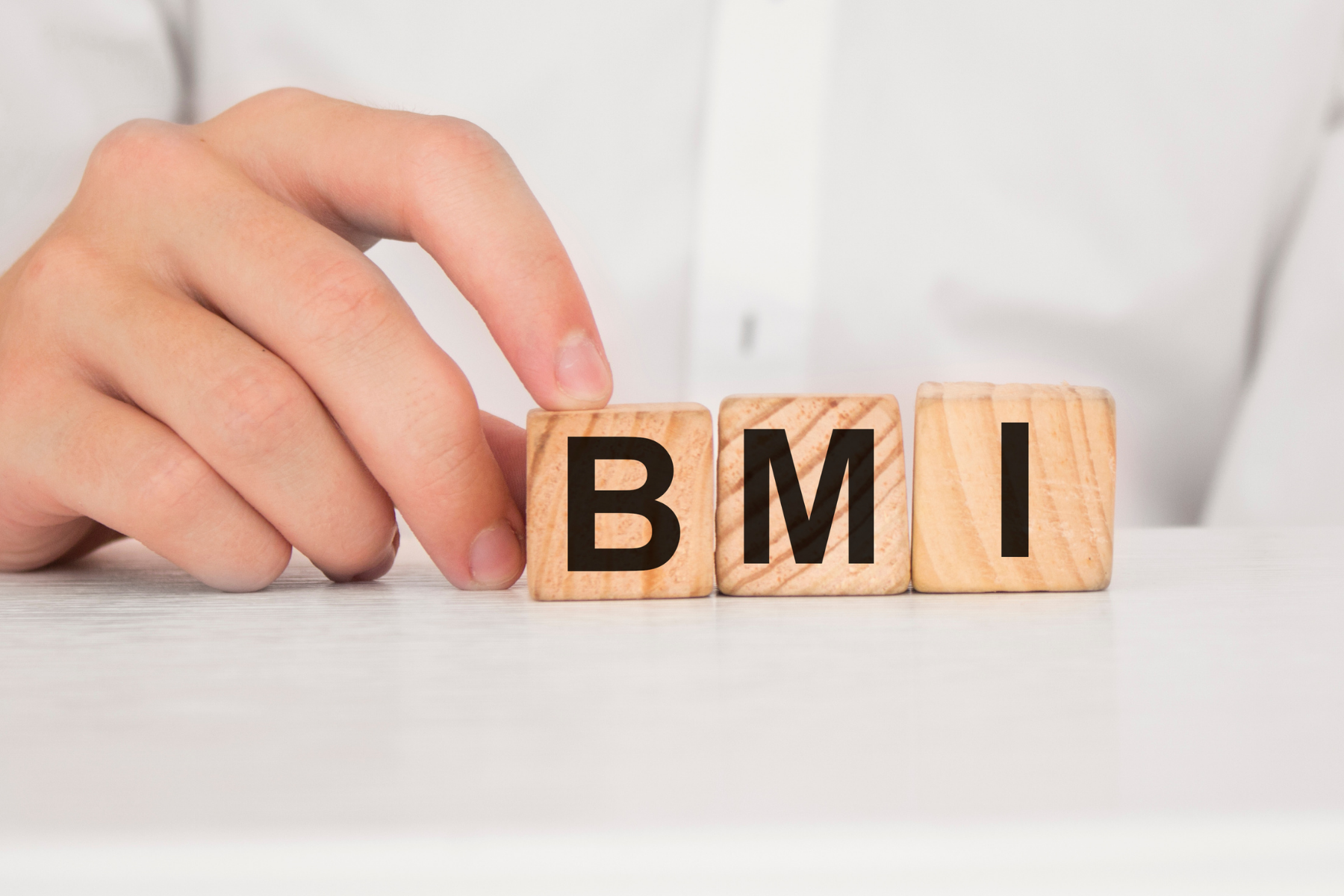 hand touching wooden blocks that spell the letters BMI for body mass index