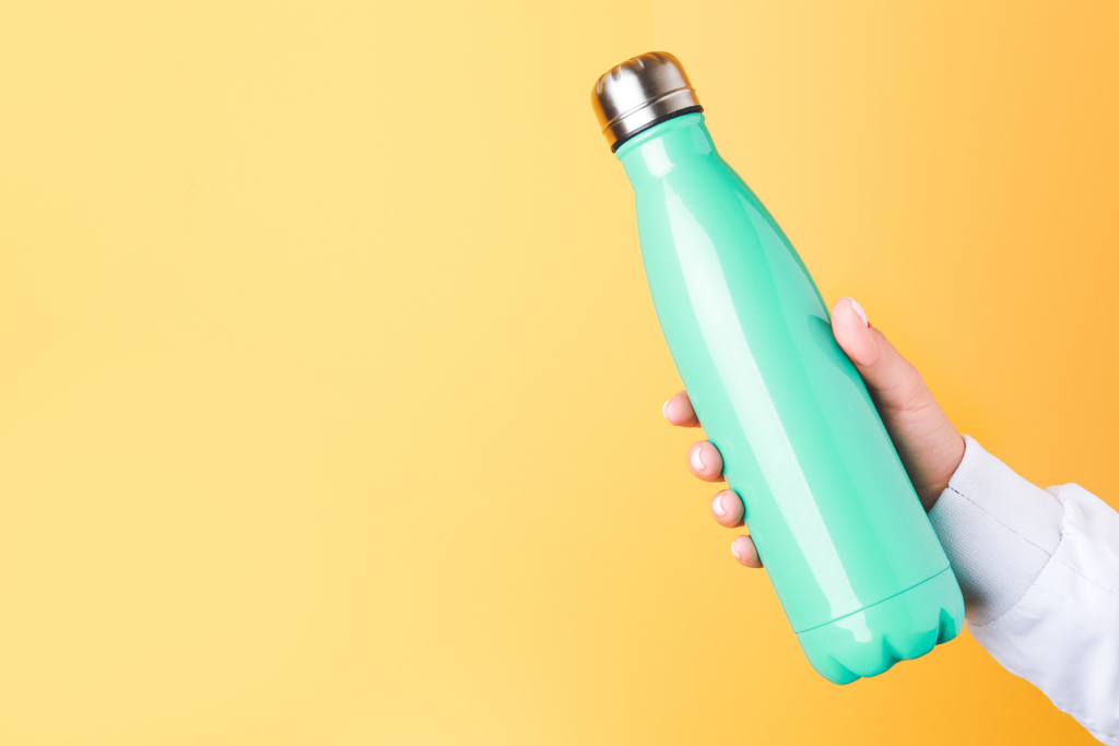 Aqua coloured swell shaped water bottle for hydration held up by a hand on the right side of the image in front of a bright yellow background.