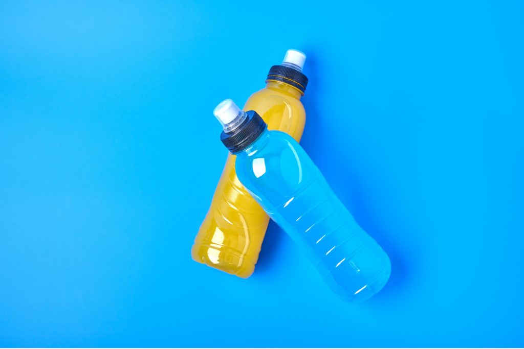Two bottles of sports drinks for hydration crossed on top of one another on a blue surface. One electrolyte drink is yellow while the other is blue.
