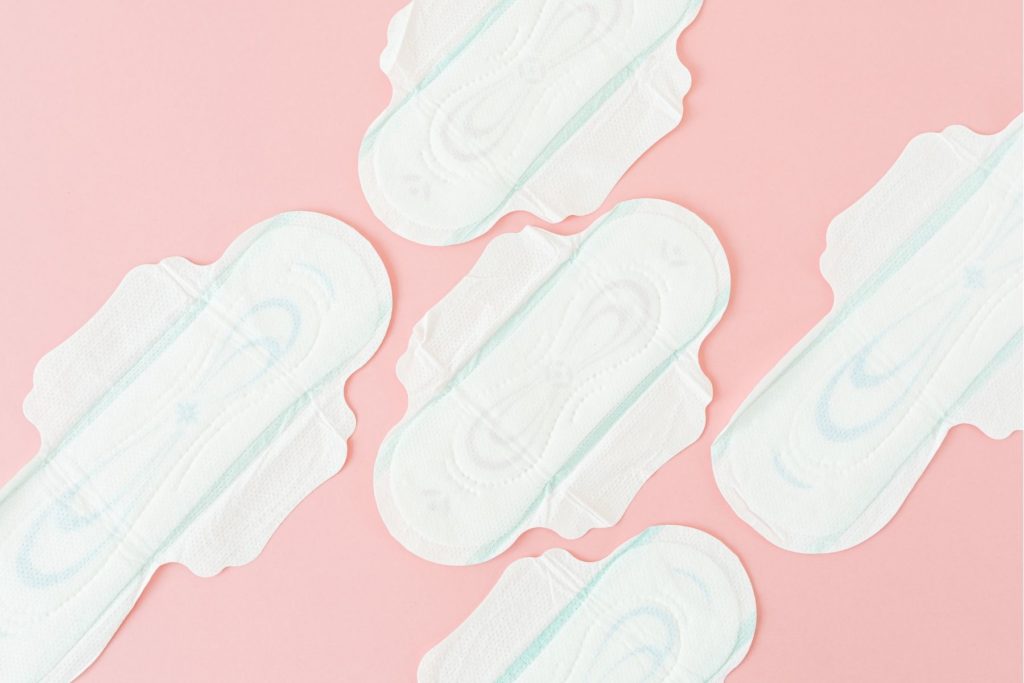 Overhead view of menstrual pads or period pads lain out flat on a light pink background.