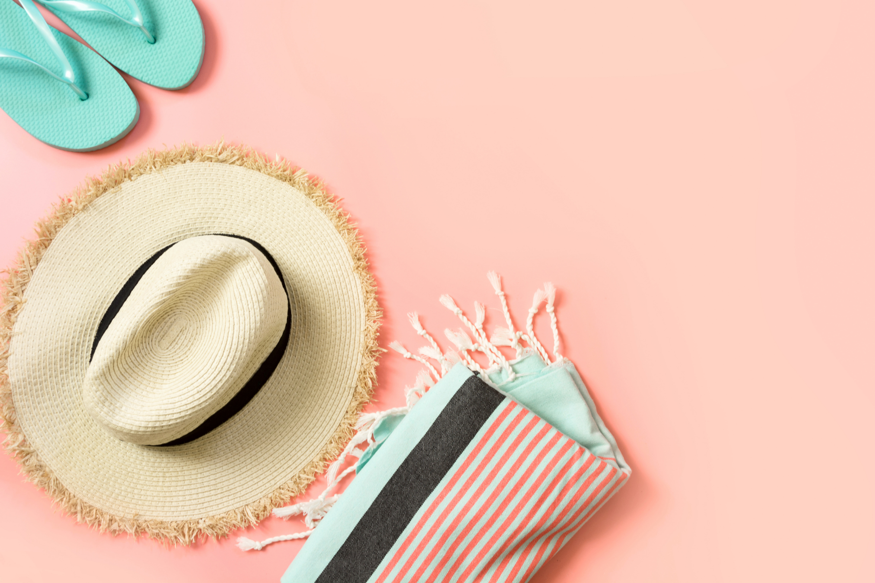 straw hat, blue flipflops and blue and pink towel on a pink summer background