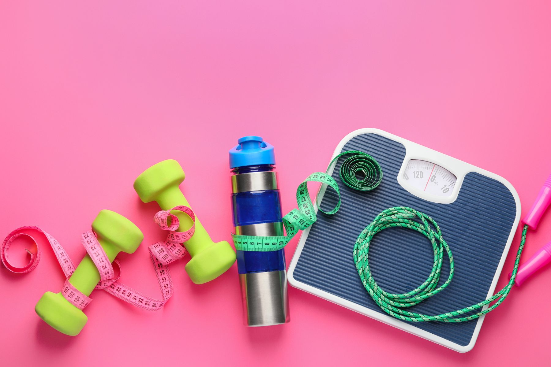 yellow dumbbells, blue water bottle, blue scale, green jump rope, against a pink background