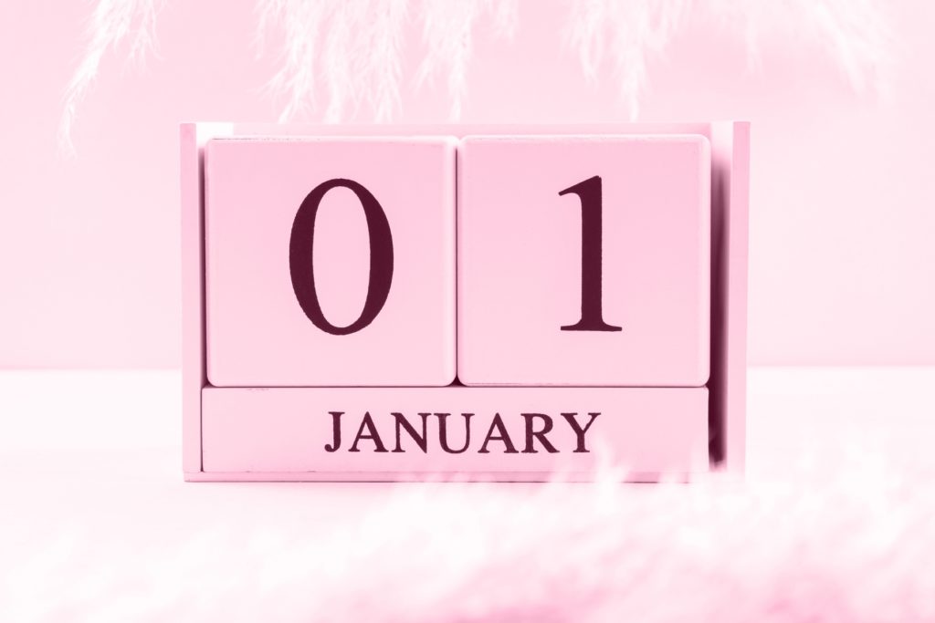Image of a pink block calendar that reads January first. The block calendar sits on a white table in front of a light pink wall.
