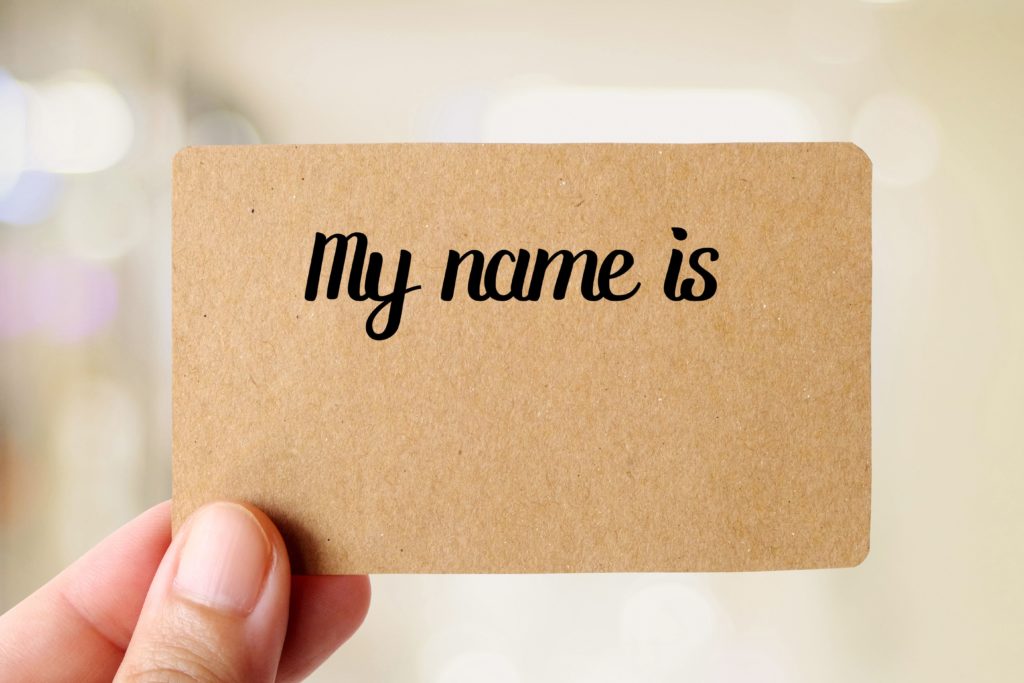 Image of fingers holding up a brown piece of paper that says "my name is". 