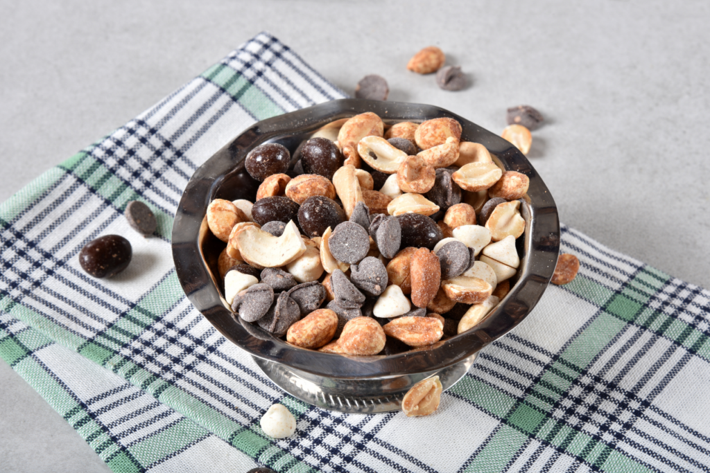 A bowl of mixed nuts and chocolate chips sits on a mint green, black and white plaid kitchen towel on a grey countertop. 