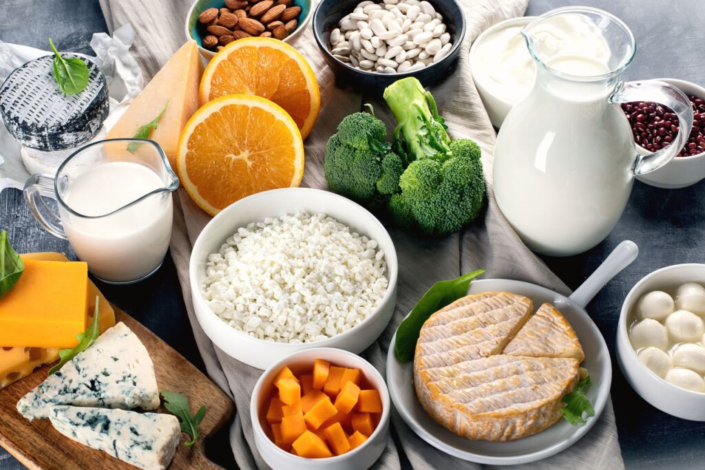 Calcium rich foods on table including broccoli, milk, cheese, and nuts. Also included in the image are oranges.
