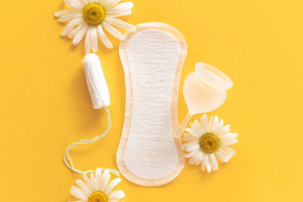 Period supplies including Panty liner, tampon, menstrual cup and 3 daisies on a yellow background.