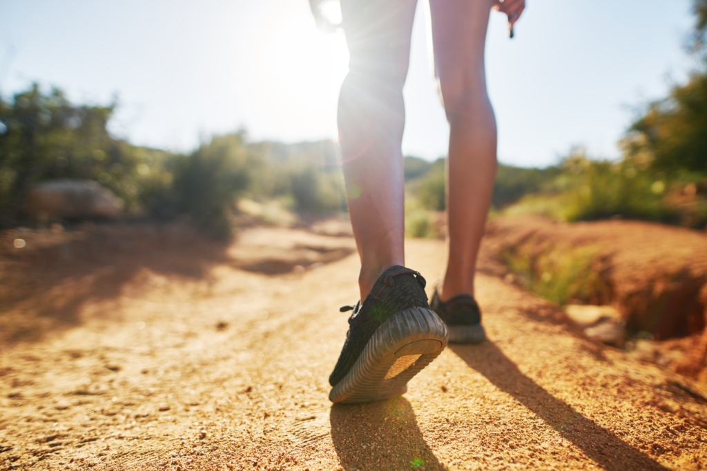 A woman's legs walking down a dirt trail. She wears black sneakers and walks away from the camera.