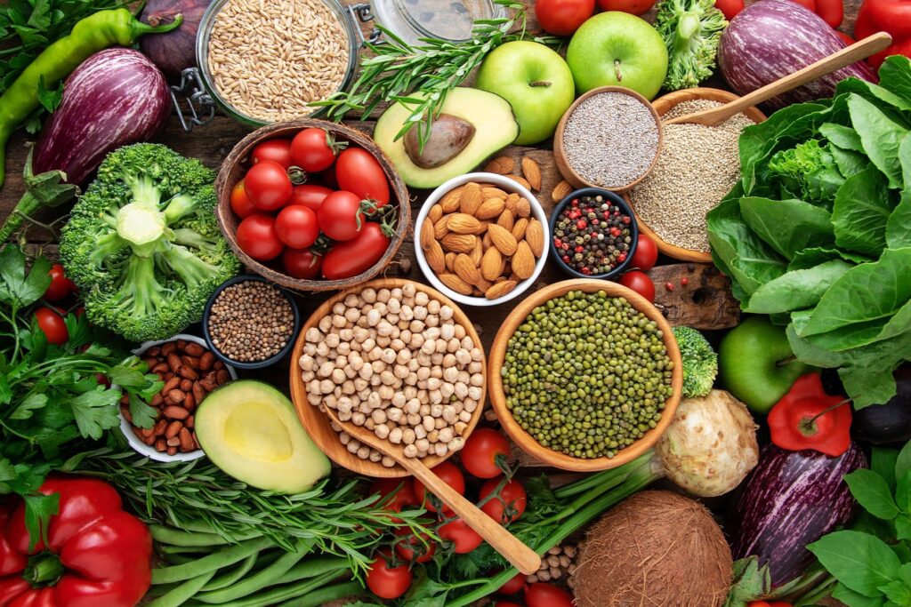 Overhead view of a spread of vegetarian foods including fruits, veggies, nuts, grains, and legumes.