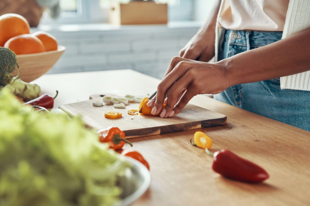 Woman's hands cutting up bell peppers on wooden cutting board that is sitting on wooden countertop for meal planning. 