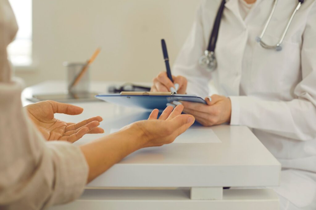 Image of a woman talking to her primary care provider who is writing on a clipboard in a white coat. 