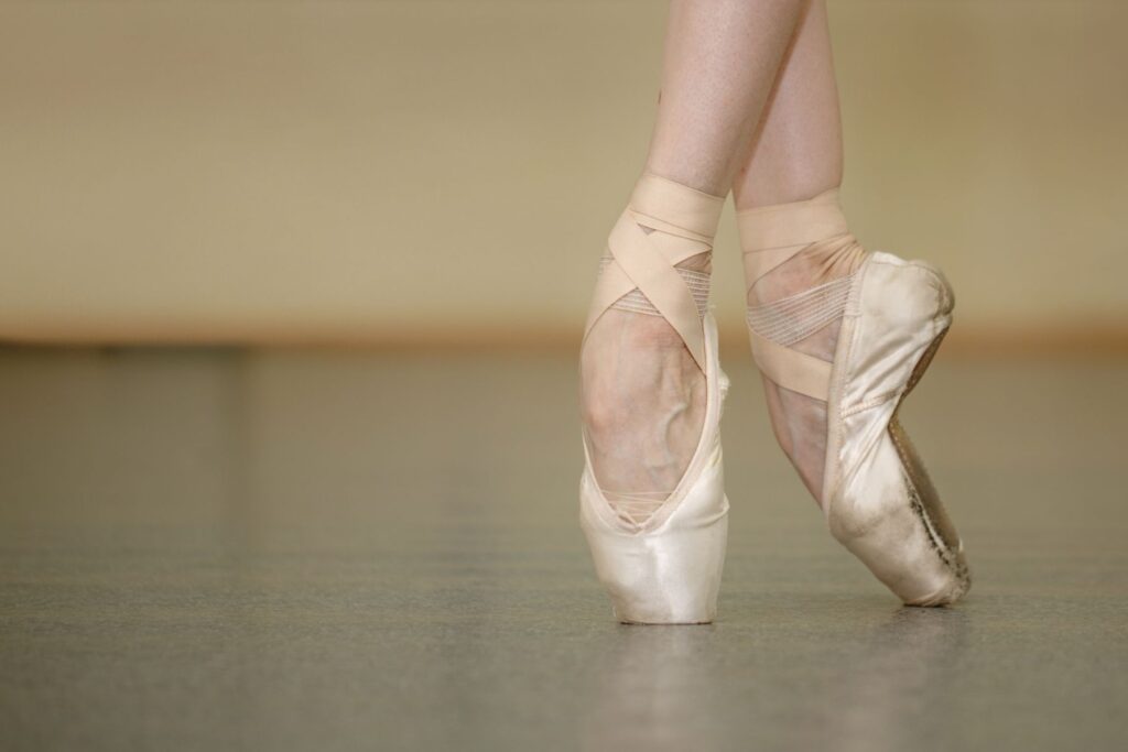 A dancers feet in pointe shoes as she is on pointe in a dance studio. 
