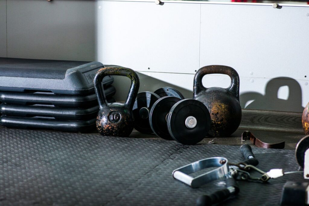 Dumbbells. kettlebells, step up steps. and cable attachments at a gym on the floor. 