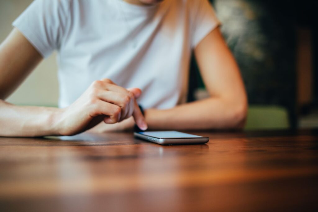 Woman sitting at wooden table with her phone on the surface as she scrolls. 