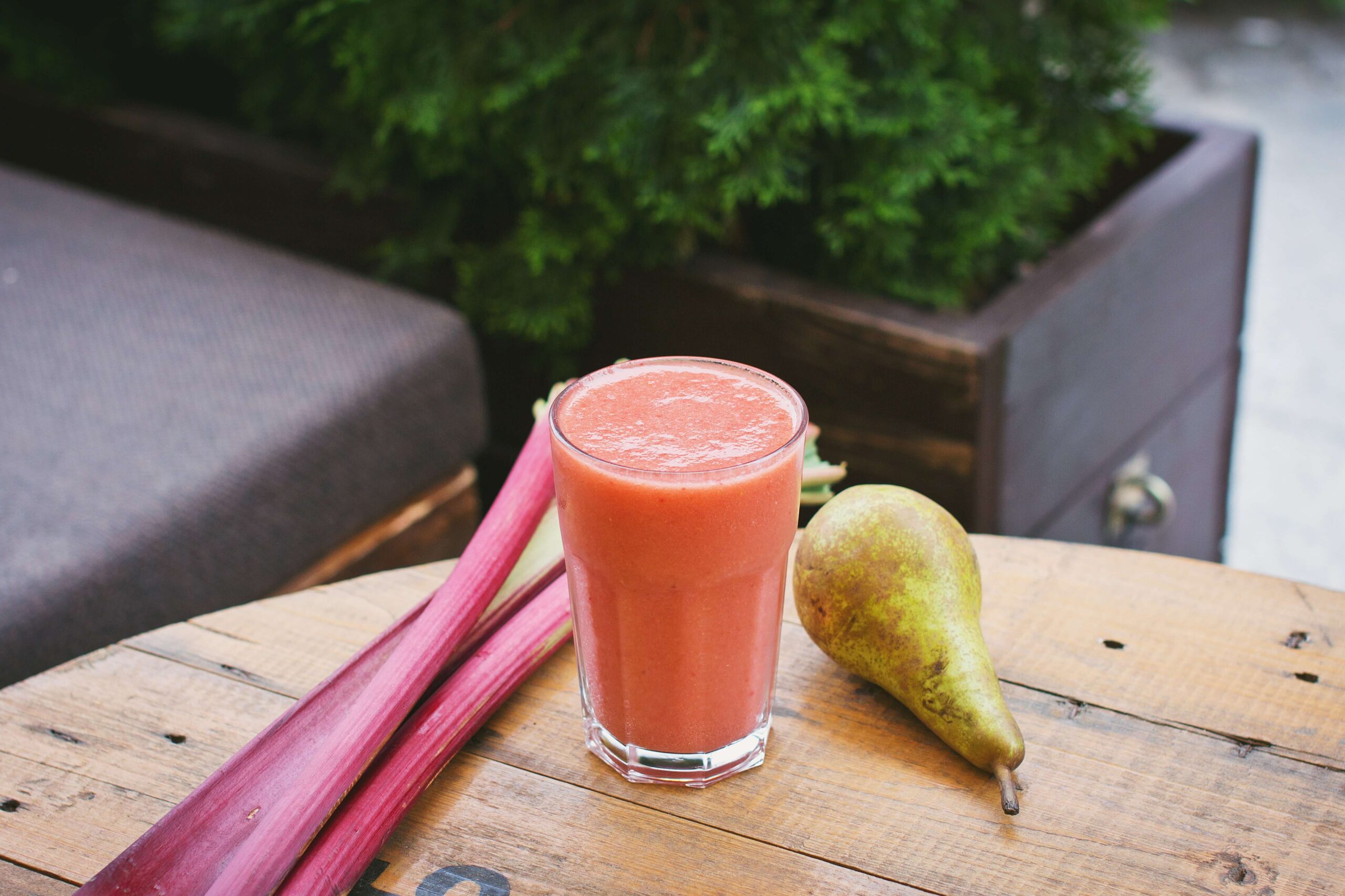 A glass of juice sits on a table outside next to rhubarb and a pear