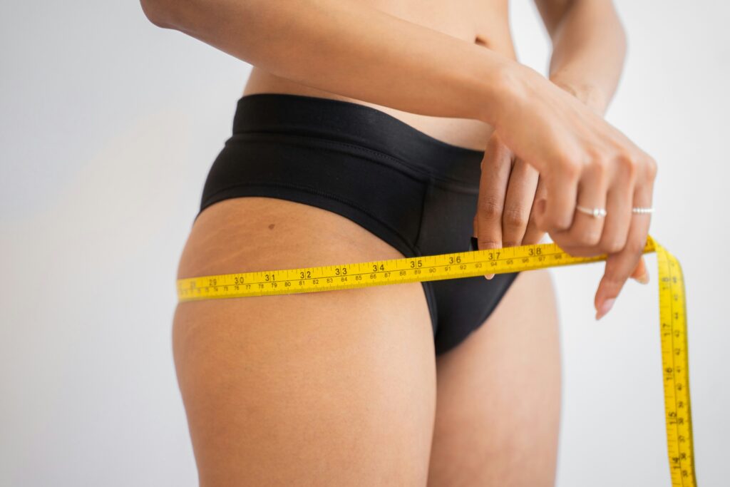 The bottom half of a woman in black underwear with a tape measure, measuring her waist