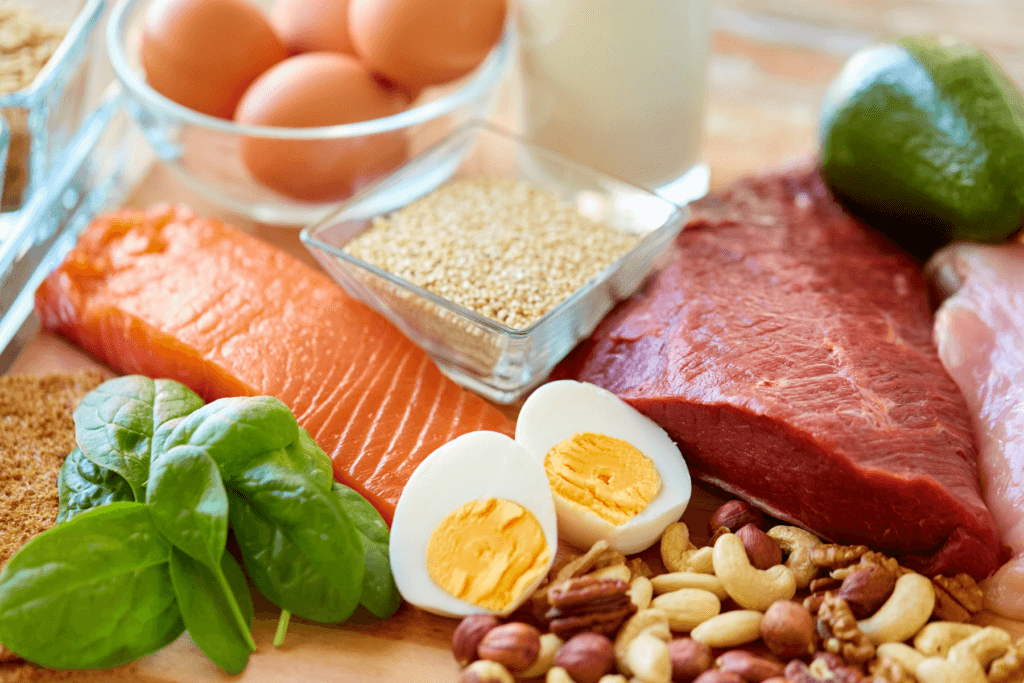 Assortment of high-protein foods including salmon, beef, eggs, quinoa, nuts, spinach, and avocado.